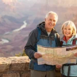A smiling senior couple wearing hiking gear holds a map at the Grand Canyon.